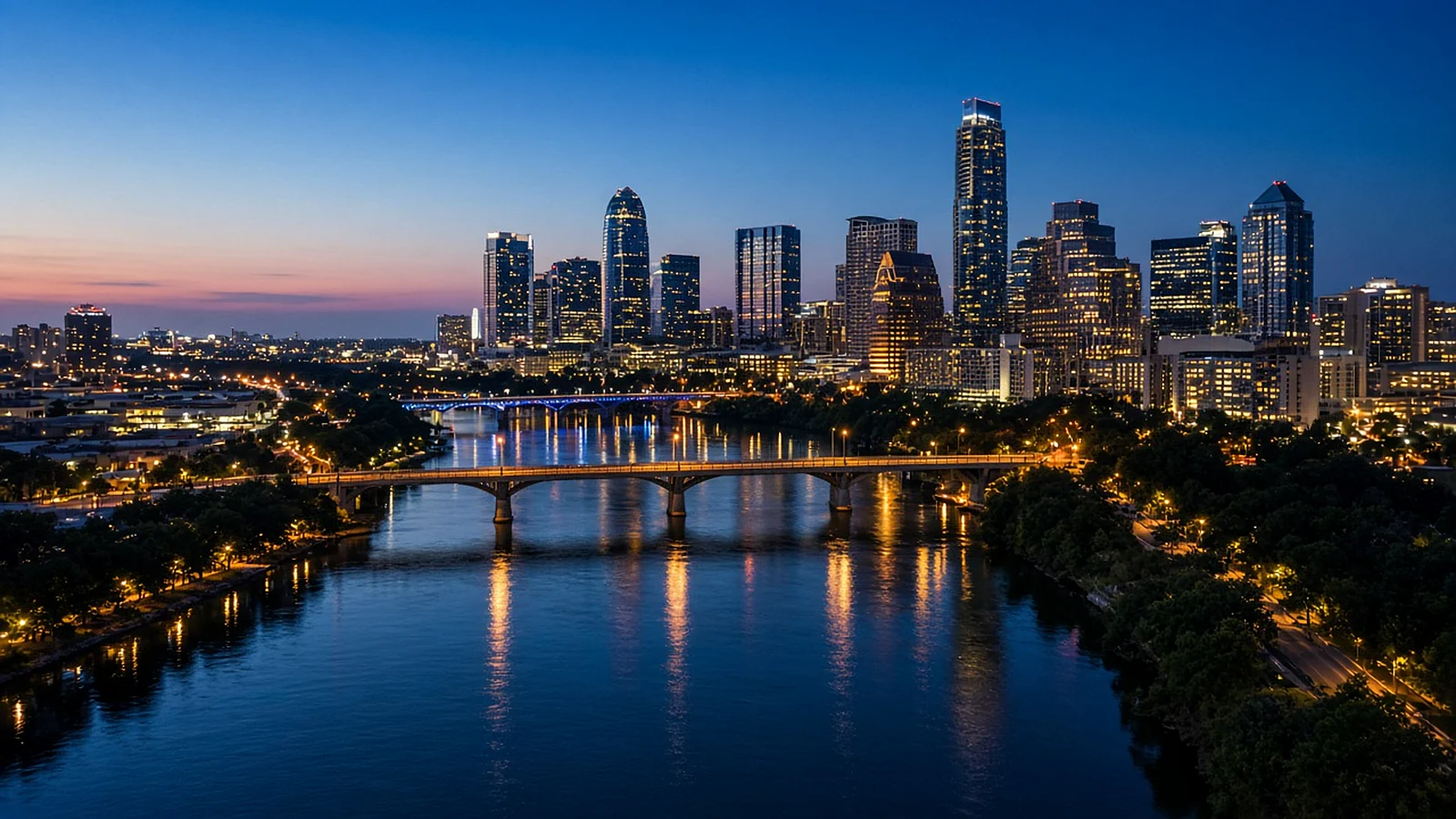 Aerial view of a downtown Texas skyline at blue hour reflected in a river with bridges glowing