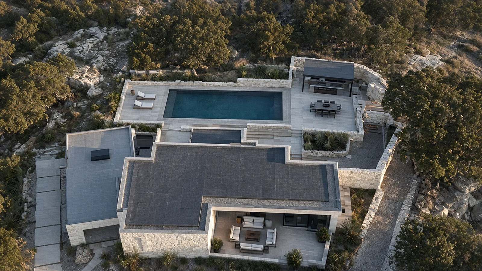Top-down aerial view of a modern home with a pool and outdoor kitchen surrounded by limestone and live oaks