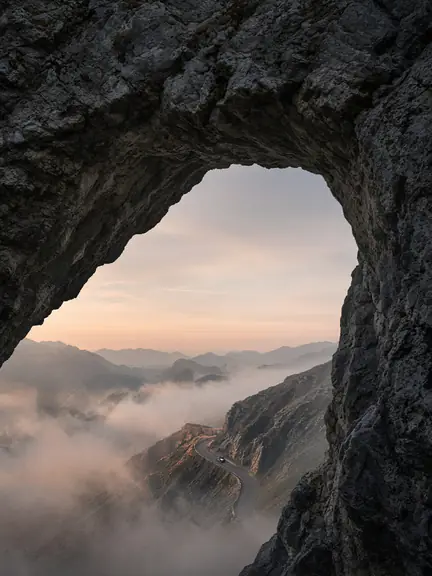 A mountain road seen through a natural rock arch at sunrise