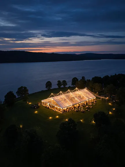 Aerial view at dusk of a glowing event tent beside a lake